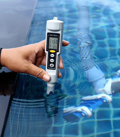 Someone holding a water testing device on the surface of a pool.